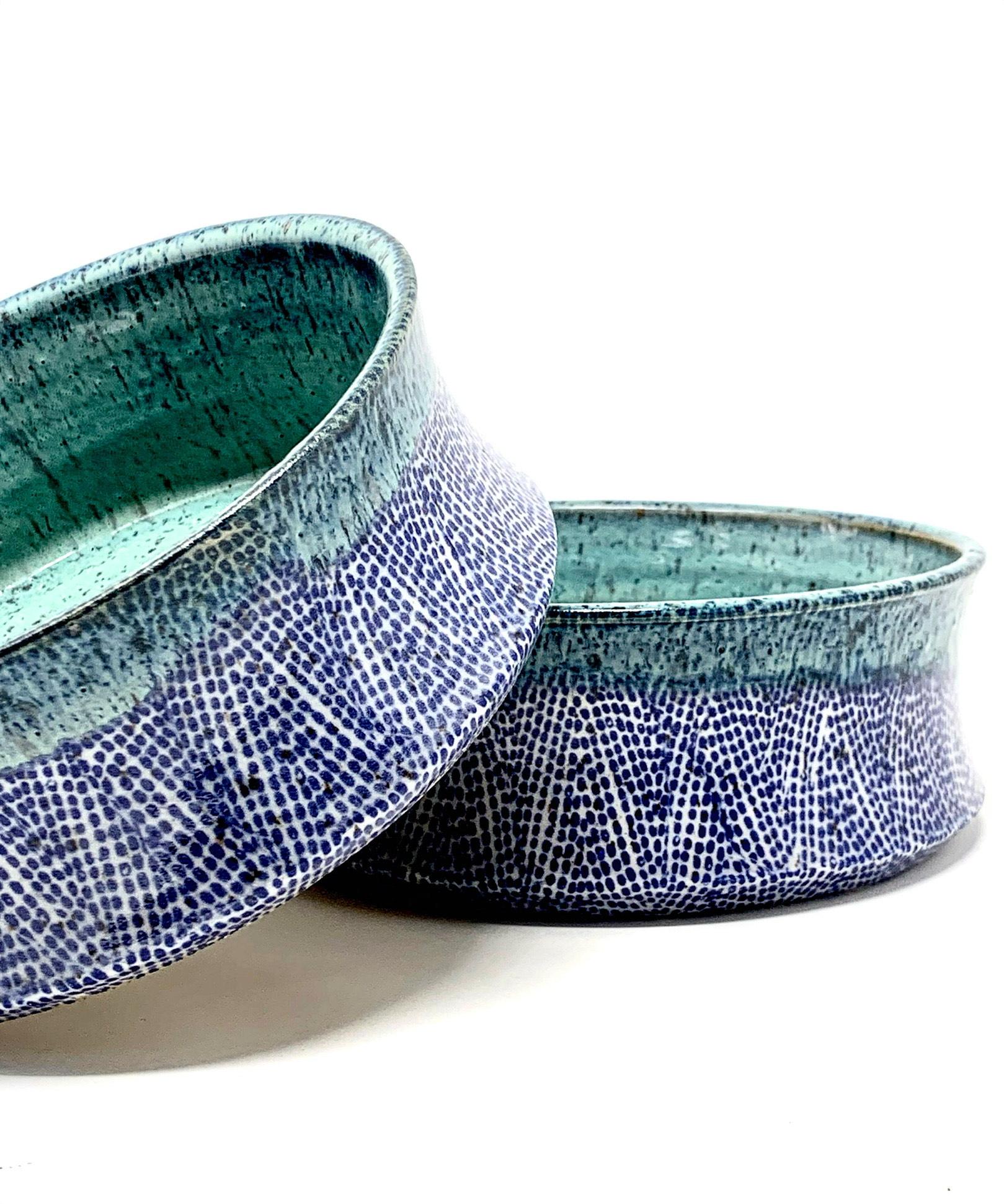 These handcrafted bowls feature a detailed speckled pattern, resembling a network of delicate coral or a close-up of a butterfly's wing. The exterior of each bowl presents a striking contrast with a serene teal glaze, suggesting a harmony between the vibrant life of coral reefs and the calm of the ocean's surface.